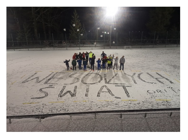 Uczestnicy zajęć sportowych na orliku i wielki napis na śniegu Wesołych Świąt